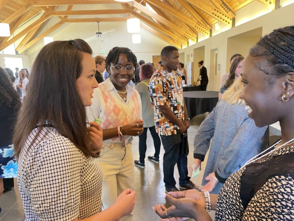 A woman talks to two high school students in a college hall,