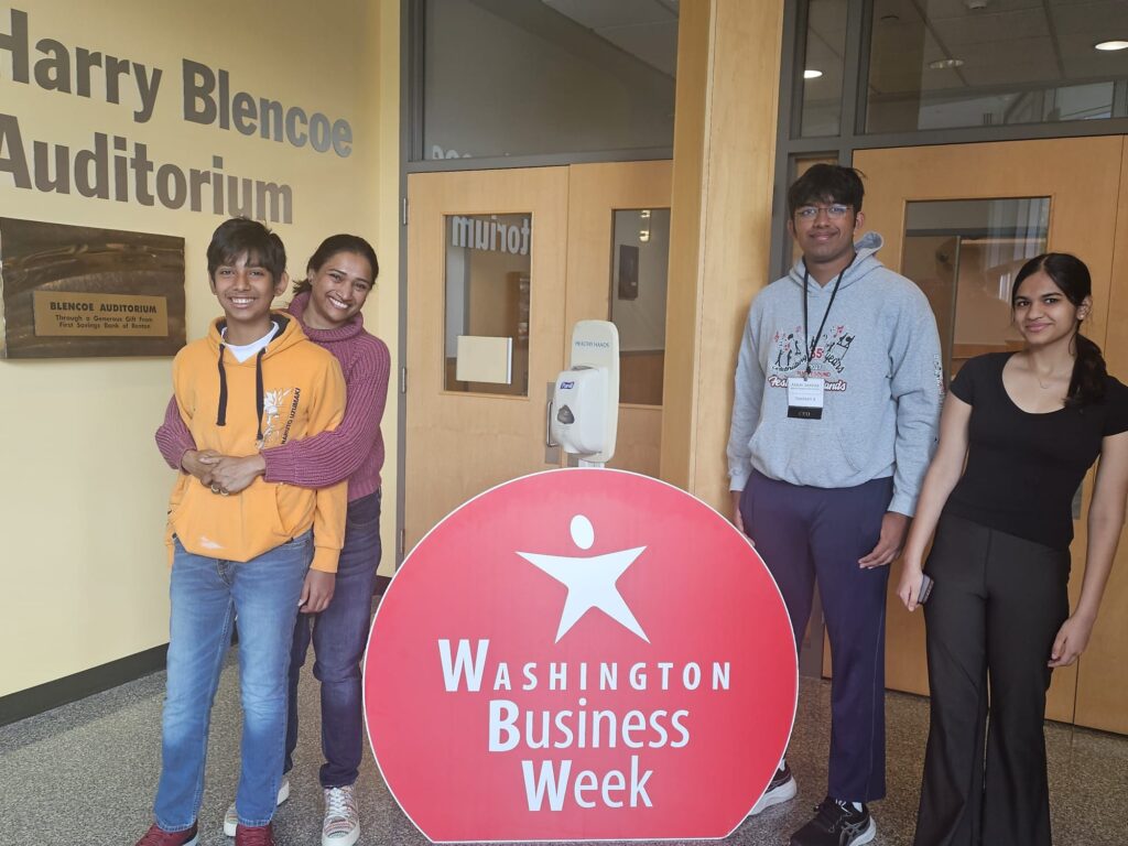 A parent hugs her child in front of a Washington Business Week sign with two other students standing nearby.