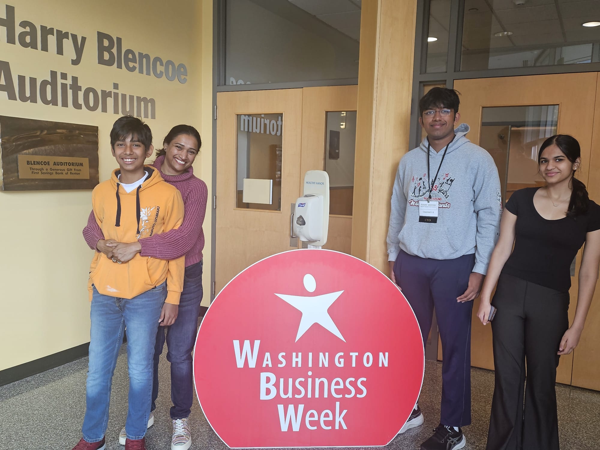 A parent hugs her child in front of a Washington Business Week sign with two other students standing nearby.