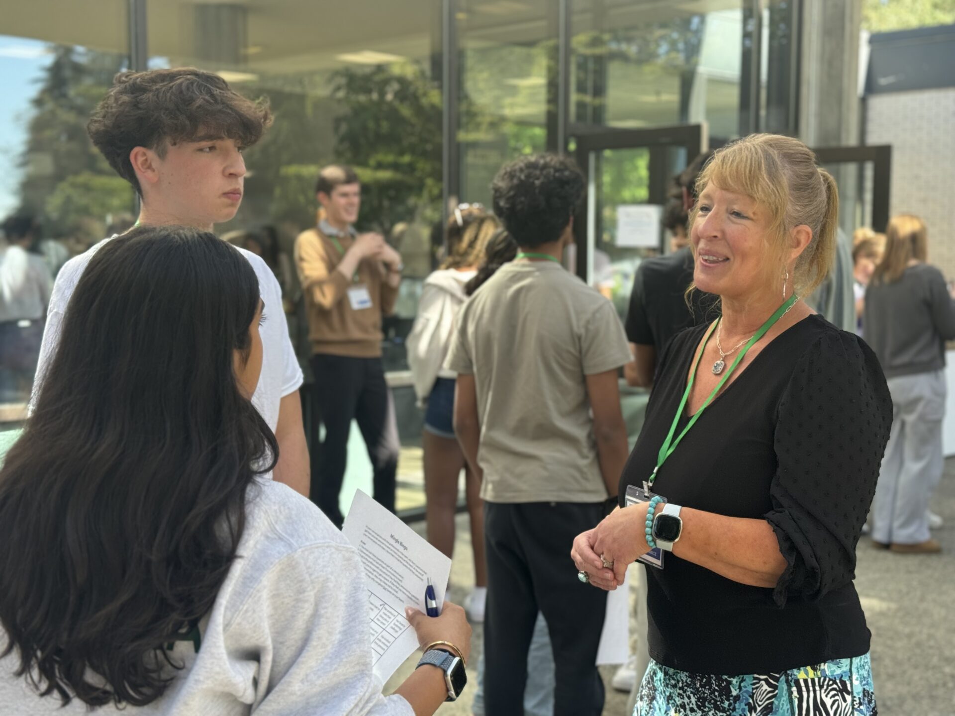 A woman stands smiling talking to two students.