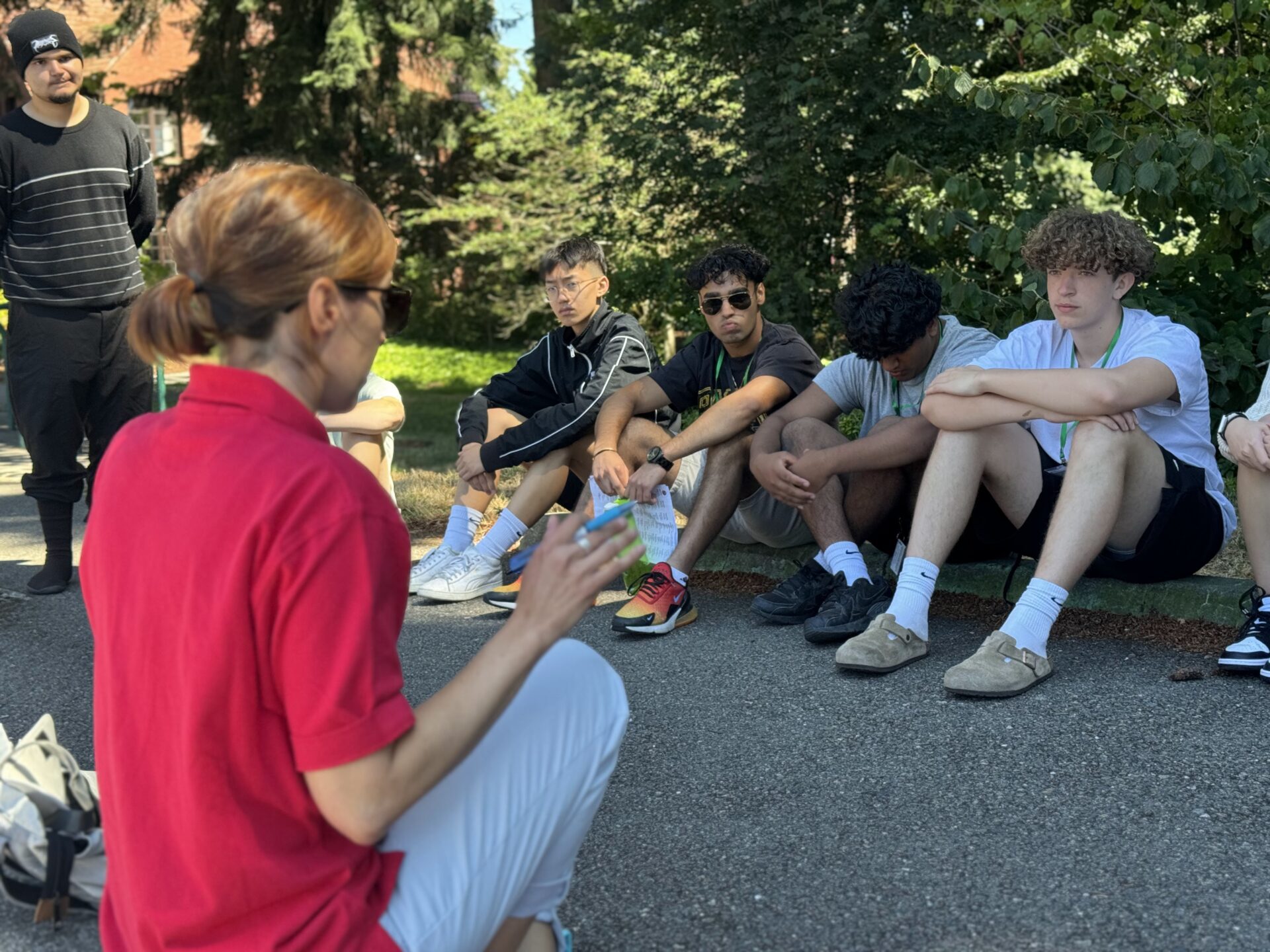 A woman sits with a group of boys on the ground.