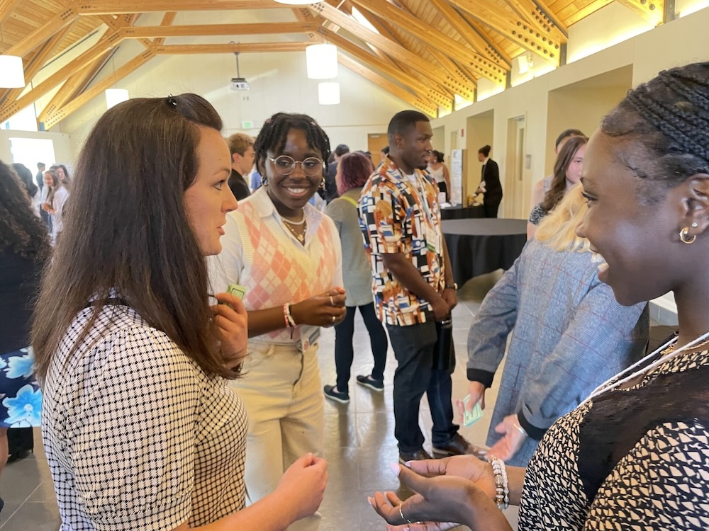 Two young black female students talk to a white adult in a brightly lit room.