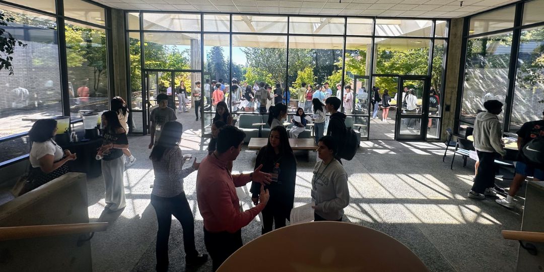 Students stand in a light. filled atrium speaking with adults. 